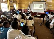 A librarian teaches school students in a school classroom online safety skills, using a whiteboard and projector for slides. 